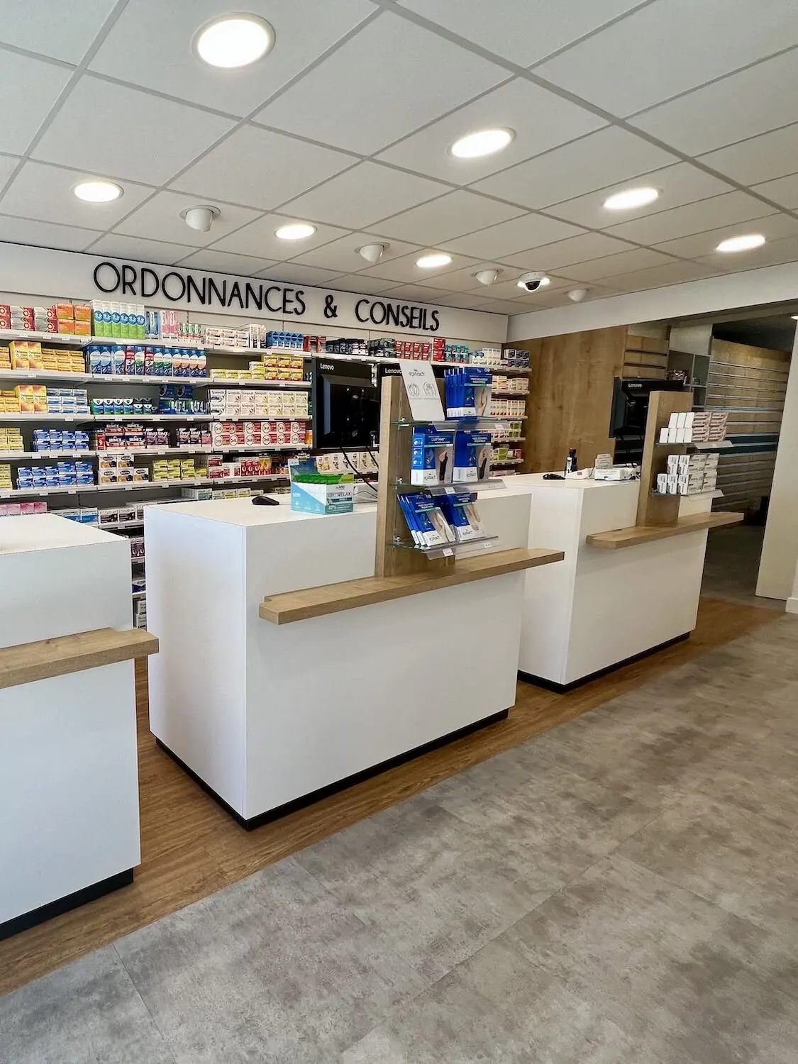Les comptoirs blancs à plateau de chêne, sous le mur « Ordonnances & Conseils » de la pharmacie